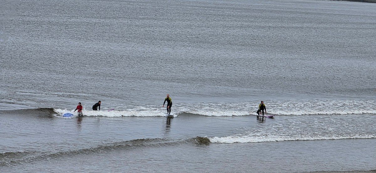 A couple of beginner surfers on a tiny wave in the middle of the beach